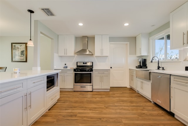 kitchen with light wood finished floors, visible vents, backsplash, wall chimney range hood, and appliances with stainless steel finishes