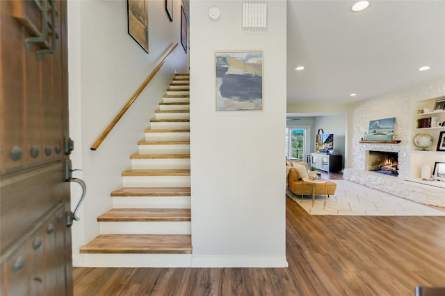 staircase featuring recessed lighting, built in shelves, wood finished floors, and a fireplace