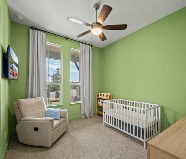 carpeted bedroom featuring a crib, a ceiling fan, and baseboards