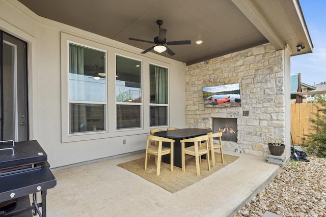 view of patio featuring outdoor dining space, a ceiling fan, fence, and an outdoor stone fireplace