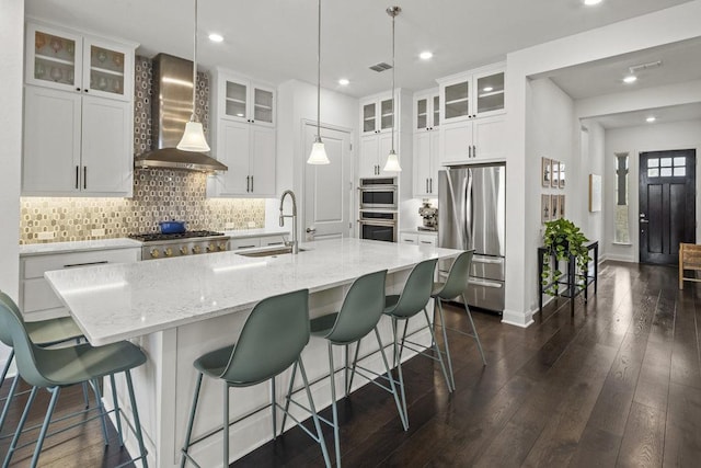 kitchen with visible vents, a sink, stainless steel appliances, wall chimney range hood, and backsplash