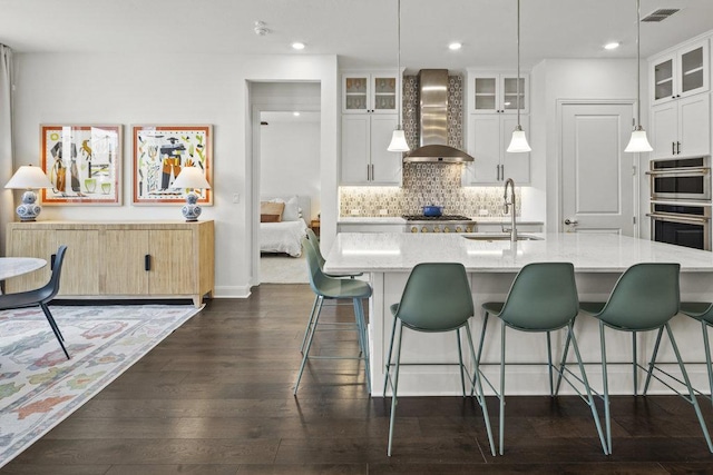 kitchen featuring visible vents, a sink, tasteful backsplash, dark wood-style floors, and wall chimney range hood