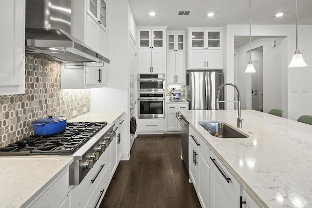 kitchen featuring visible vents, white cabinets, stainless steel appliances, wall chimney exhaust hood, and a sink