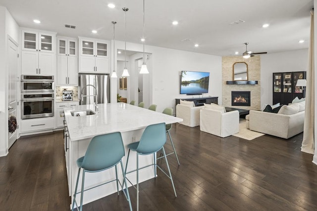 kitchen featuring light stone counters, visible vents, dark wood-style flooring, a sink, and appliances with stainless steel finishes