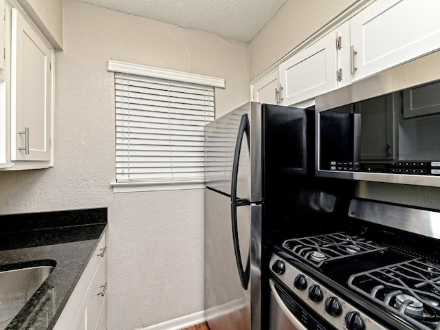 kitchen with dark stone countertops, a sink, white cabinets, a textured ceiling, and a textured wall