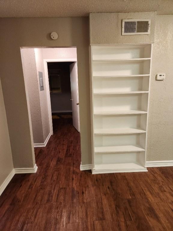 corridor featuring built in shelves, wood finished floors, visible vents, baseboards, and a textured ceiling