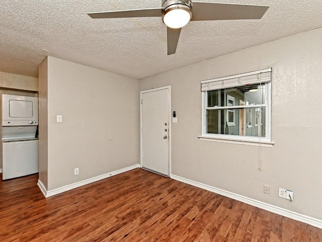 unfurnished room featuring wood finished floors, baseboards, ceiling fan, stacked washer / drying machine, and a textured ceiling