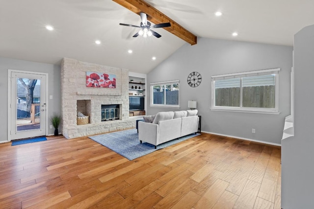 living room with a ceiling fan, light wood-style floors, a fireplace, baseboards, and vaulted ceiling with beams