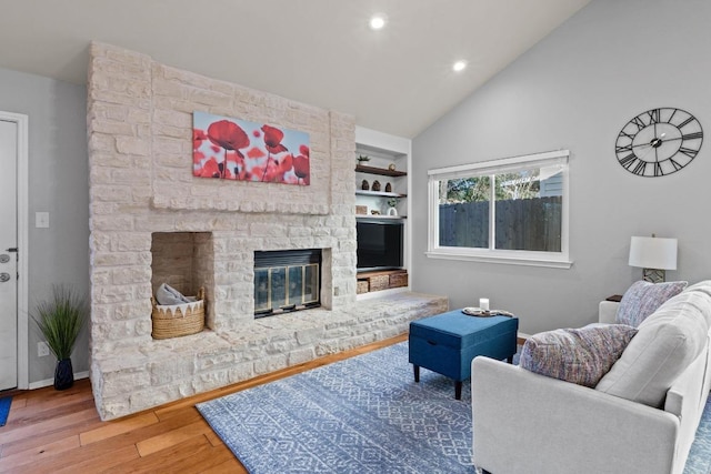 living area featuring built in shelves, wood finished floors, baseboards, a fireplace, and vaulted ceiling