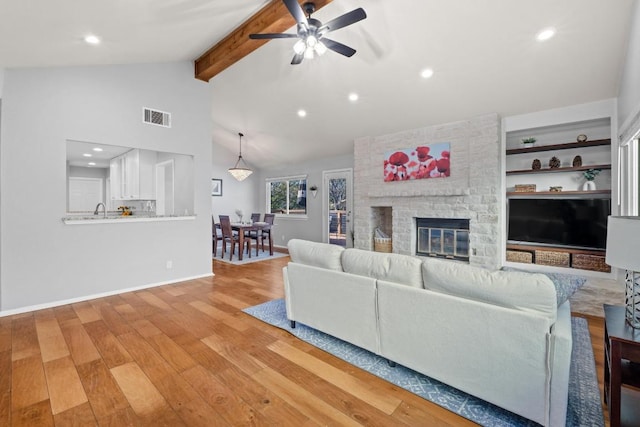 living area with wood finished floors, beamed ceiling, visible vents, baseboards, and a brick fireplace