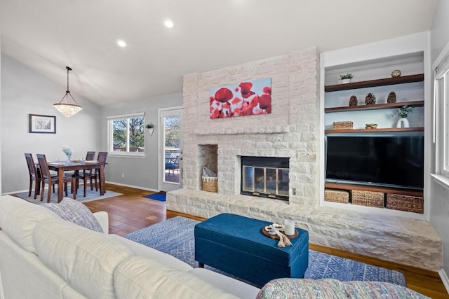 living room with a stone fireplace, vaulted ceiling, wood finished floors, and baseboards