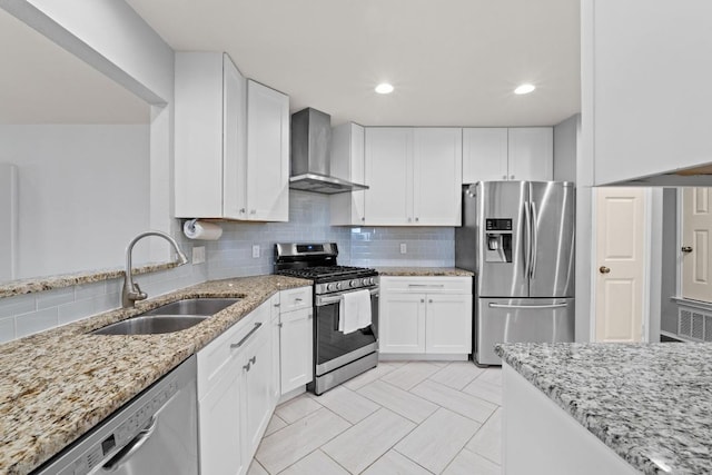 kitchen featuring light stone counters, a sink, stainless steel appliances, wall chimney exhaust hood, and backsplash