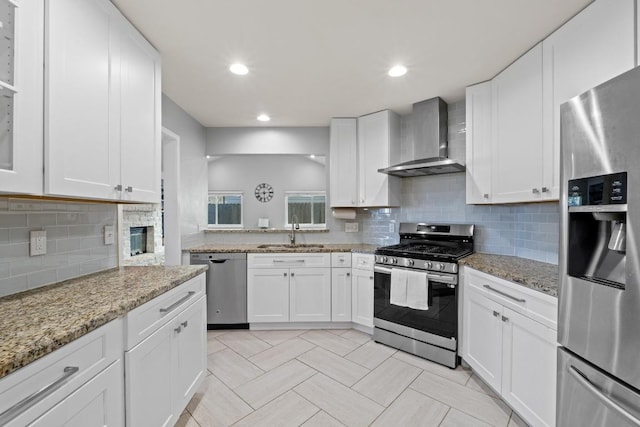 kitchen featuring tasteful backsplash, appliances with stainless steel finishes, white cabinets, wall chimney exhaust hood, and a sink