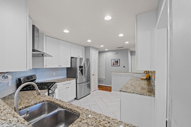 kitchen featuring a sink, light stone counters, stainless steel appliances, wall chimney exhaust hood, and white cabinets