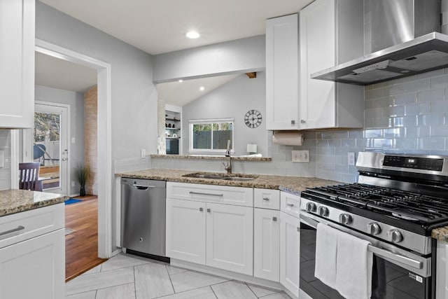 kitchen with a sink, light stone counters, stainless steel appliances, wall chimney exhaust hood, and lofted ceiling