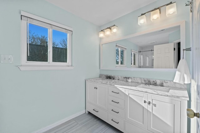 bathroom featuring double vanity, walk in shower, baseboards, and a sink