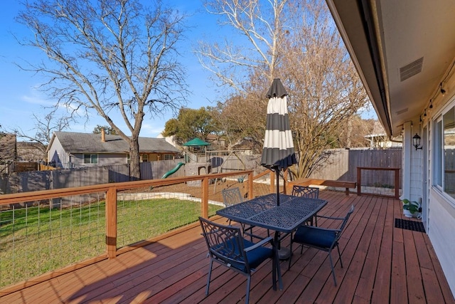 wooden terrace featuring visible vents, outdoor dining area, a playground, and a fenced backyard