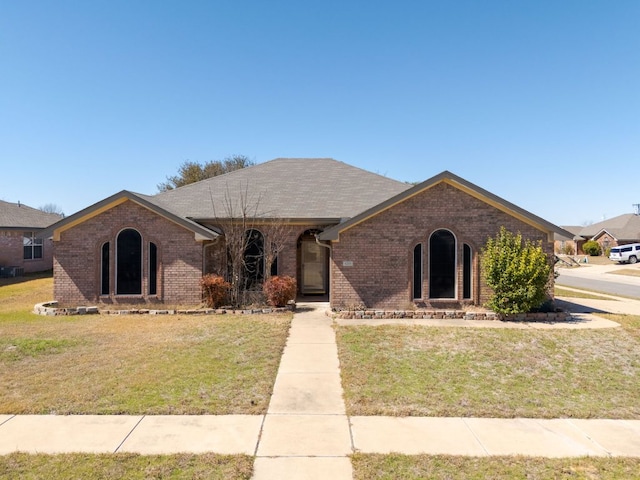 view of front of house with a front yard, brick siding, and a shingled roof