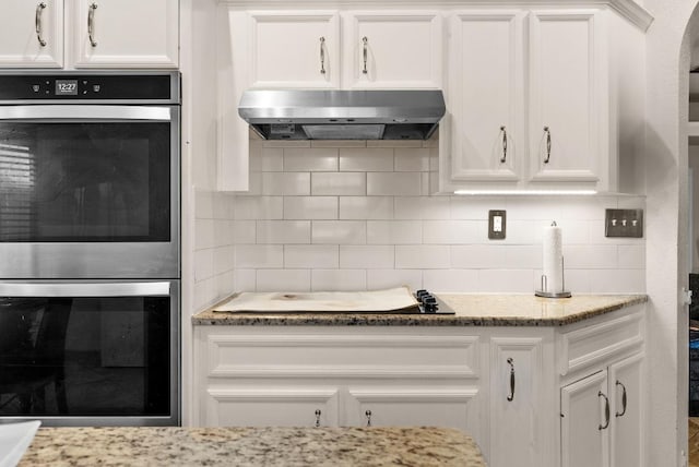 kitchen with double oven, range hood, white cabinetry, and decorative backsplash