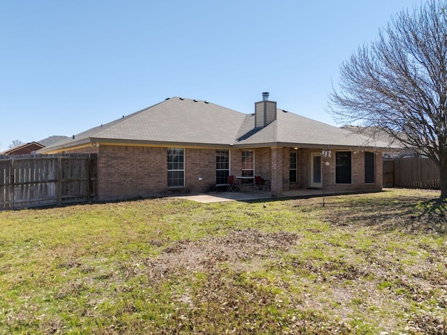 back of property with brick siding, fence, a lawn, a chimney, and a patio