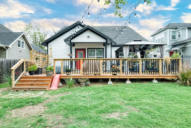 rear view of house with fence, a wooden deck, a yard, a shingled roof, and a gazebo