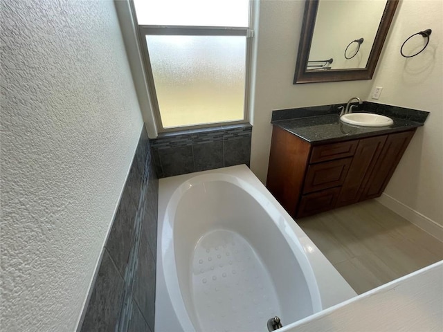 bathroom with a tub, vanity, and a textured wall