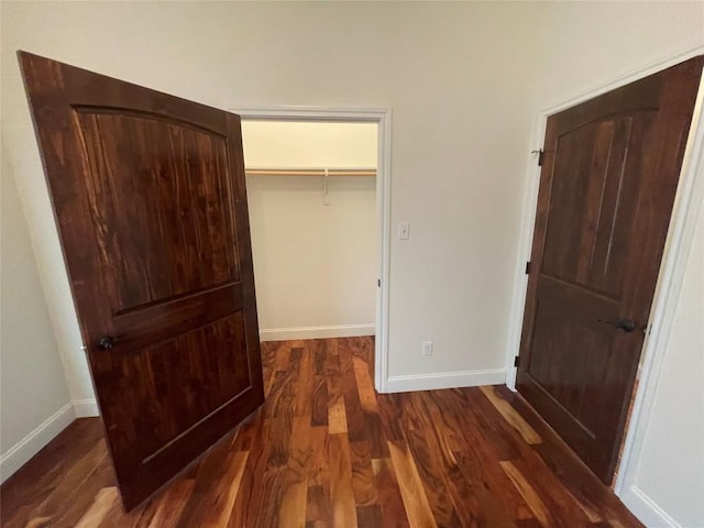 unfurnished bedroom with dark wood finished floors, a spacious closet, and baseboards