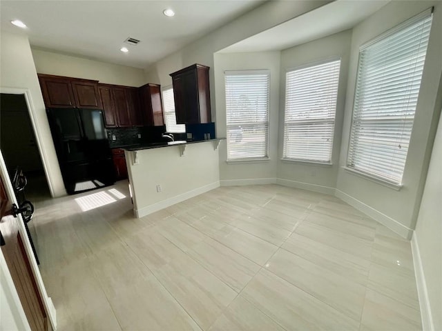 kitchen featuring a breakfast bar area, visible vents, a peninsula, tasteful backsplash, and black refrigerator with ice dispenser