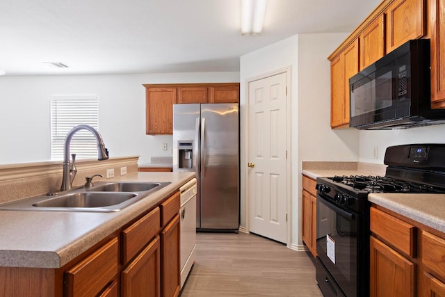 kitchen with brown cabinetry, visible vents, light wood-style flooring, a sink, and black appliances