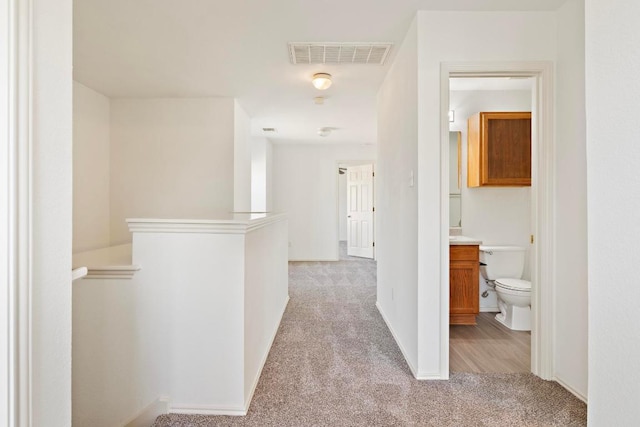 hallway with visible vents, light carpet, baseboards, and an upstairs landing