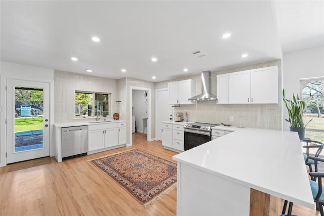 kitchen with visible vents, decorative backsplash, appliances with stainless steel finishes, wall chimney exhaust hood, and a sink