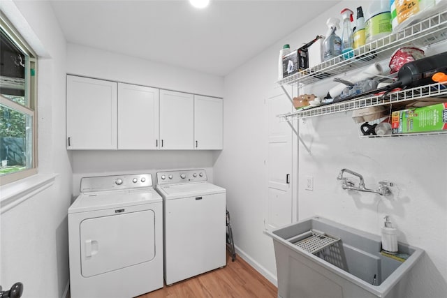 laundry area featuring light wood-type flooring, a sink, cabinet space, baseboards, and washing machine and clothes dryer