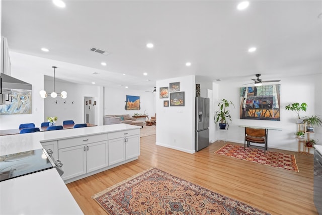 kitchen featuring light wood finished floors, open floor plan, recessed lighting, stainless steel refrigerator with ice dispenser, and white cabinets