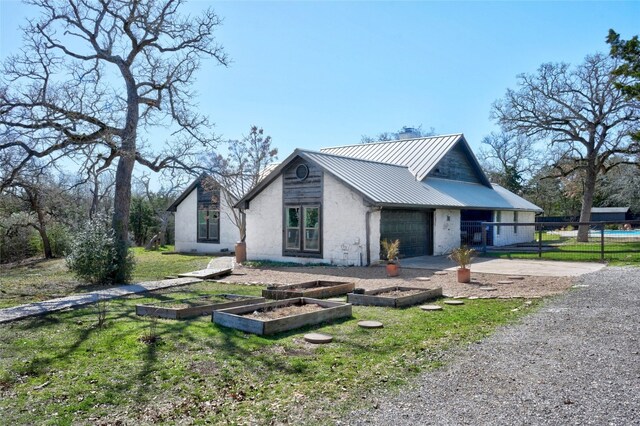 view of home's exterior featuring driveway, a standing seam roof, fence, a vegetable garden, and metal roof