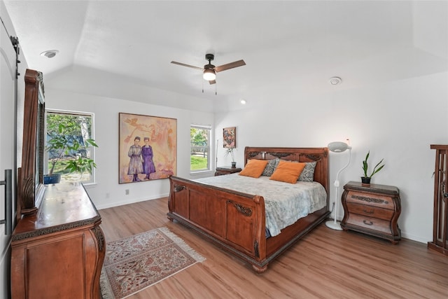 bedroom featuring ceiling fan, baseboards, light wood-type flooring, a barn door, and lofted ceiling