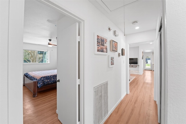 corridor featuring visible vents, baseboards, attic access, and light wood-style flooring