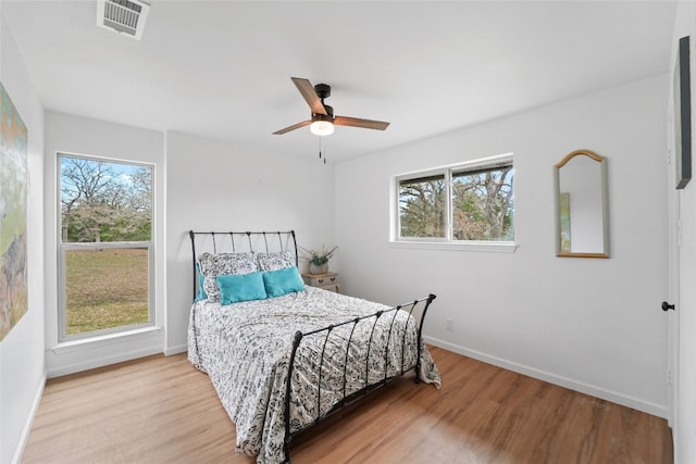 bedroom with multiple windows, wood finished floors, visible vents, and baseboards