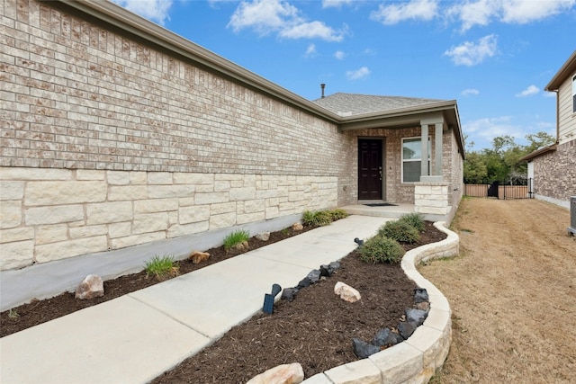 view of front of home with stone siding, brick siding, roof with shingles, and fence