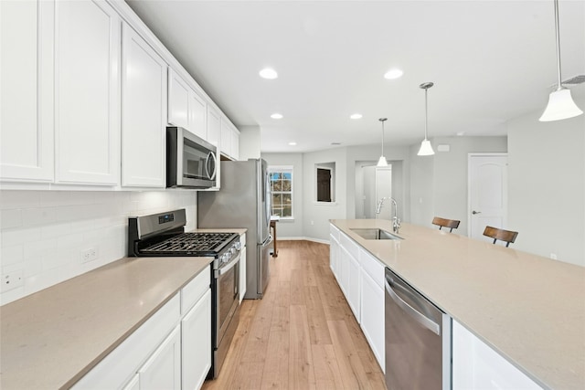 kitchen with a sink, tasteful backsplash, stainless steel appliances, white cabinets, and light wood finished floors