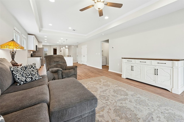 living room featuring light wood-type flooring, recessed lighting, baseboards, a raised ceiling, and ceiling fan