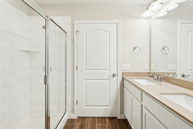 bathroom with double vanity, a shower stall, wood finish floors, and a sink