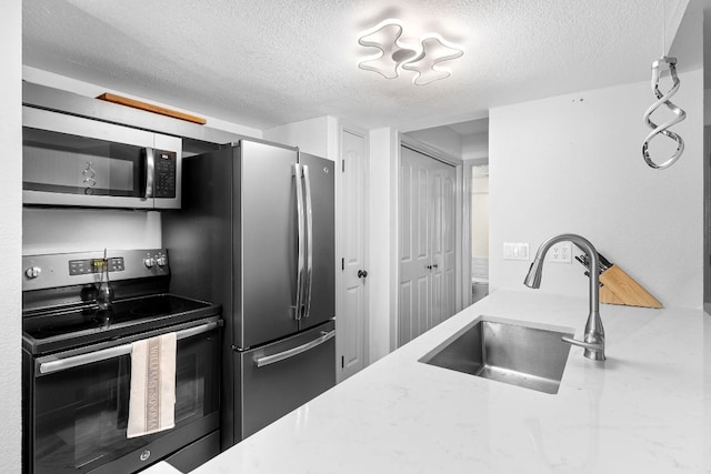 kitchen with a sink, light stone countertops, a textured ceiling, and appliances with stainless steel finishes