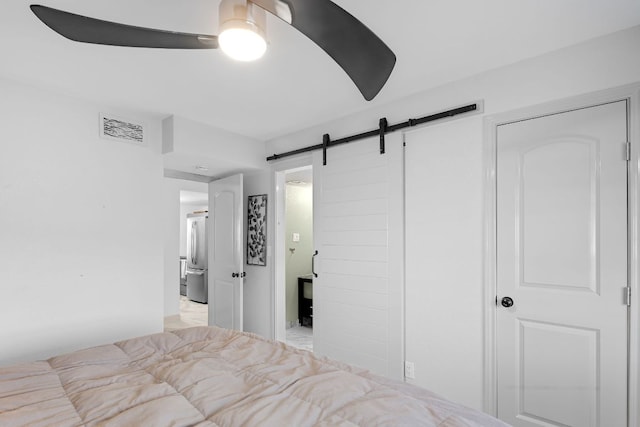 bedroom with visible vents, stainless steel fridge, a barn door, and ceiling fan