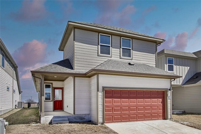 traditional-style home featuring concrete driveway, an attached garage, central AC, and a shingled roof