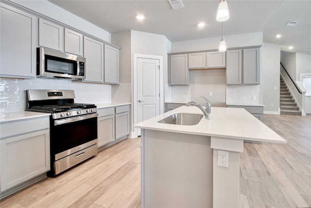 kitchen featuring gray cabinets, appliances with stainless steel finishes, light wood-style floors, and a sink