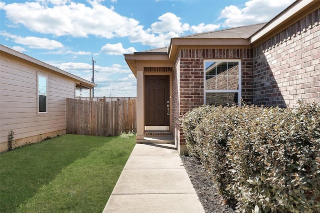 property entrance with brick siding, a lawn, and fence