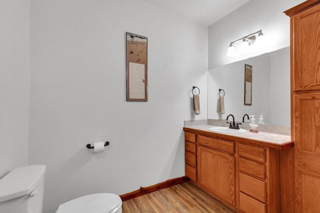 half bath featuring vanity, toilet, wood finished floors, and baseboards