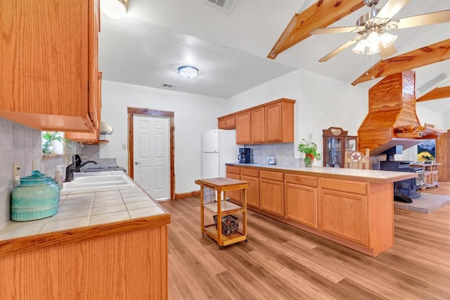 kitchen with tile countertops, a peninsula, freestanding refrigerator, a sink, and light wood-type flooring