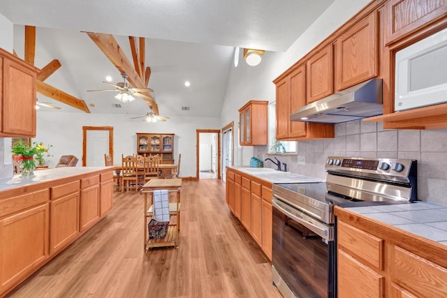 kitchen with electric range, light wood-type flooring, under cabinet range hood, tile countertops, and vaulted ceiling with beams