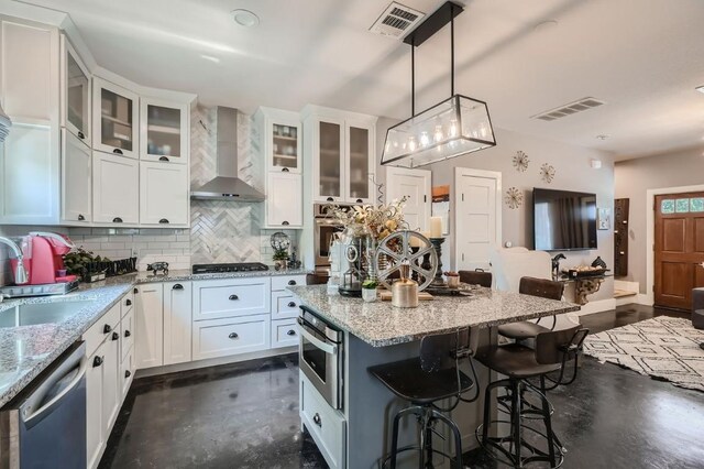 kitchen with wall chimney range hood, visible vents, a sink, stainless steel appliances, and a kitchen breakfast bar